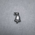 The small oxidised silver bell charm laid flat, bail to the top left.