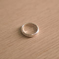 Classic polished sterling silver band ring with milgrain edges, lying on a pale wooden surface.