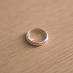 Classic polished sterling silver band ring with milgrain edges, lying on a pale wooden surface.