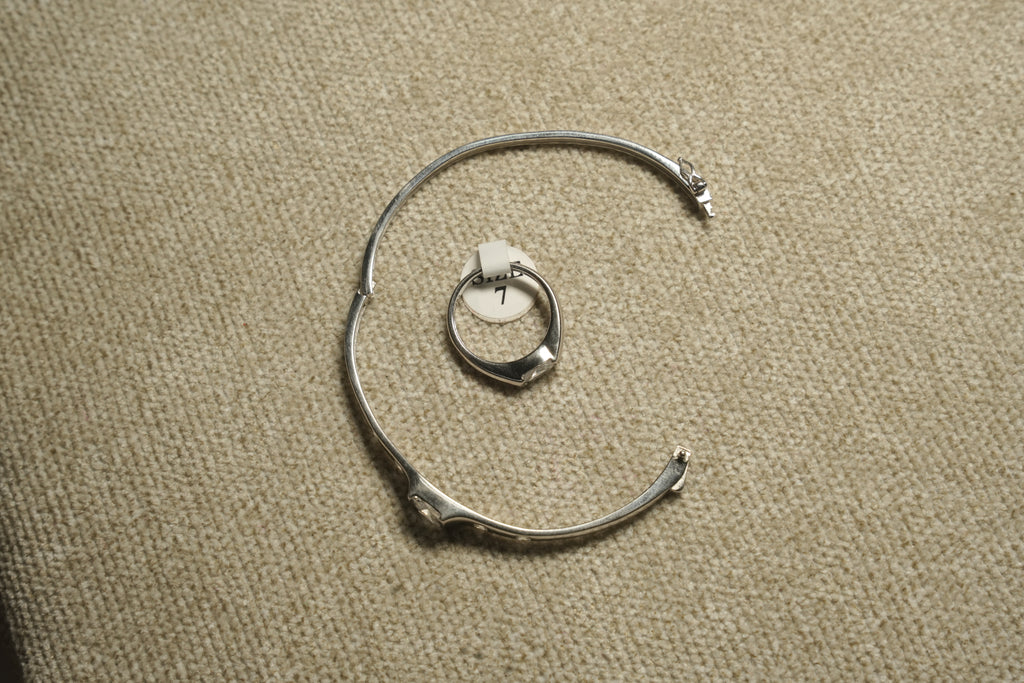 Sterling silver cubic zirconia ring on its size tag, framed by a silver bangle used as a prop on woven fabric.
