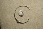Sterling silver cubic zirconia ring on its size tag, framed by a silver bangle used as a prop on woven fabric.