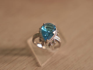 Sterling silver cocktail ring with a pear shaped sky blue glass stone in a halo, with tiny bezel drops below.