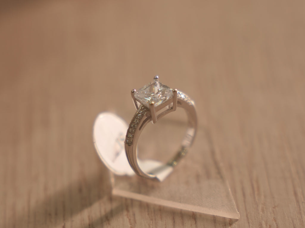 The square American Diamond solitaire ring standing upright on a clear block.