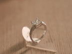 The square American Diamond solitaire ring standing upright on a clear block.