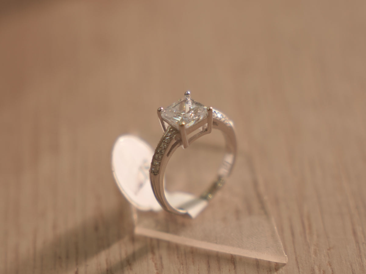The square American Diamond solitaire ring standing upright on a clear block.