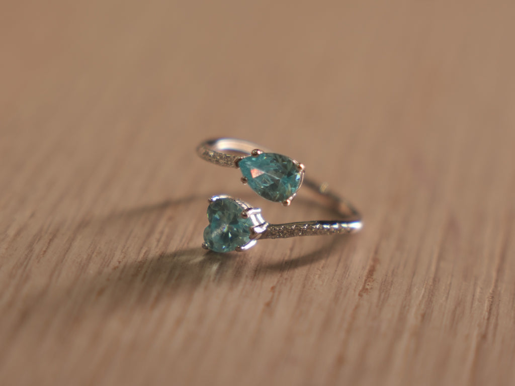 Sterling silver bypass ring with a sky blue pear shaped glass stone and a blue heart at the crossing.
