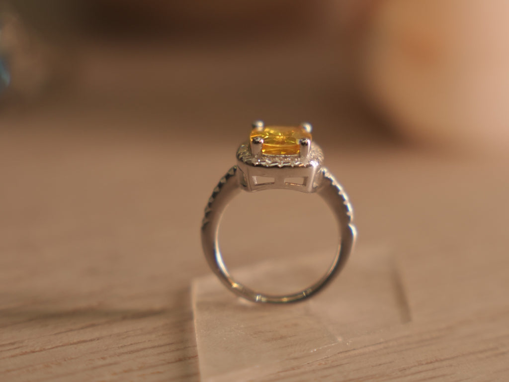 Sterling silver halo ring with a cushion cut vivid yellow glass stone in a four prong setting.