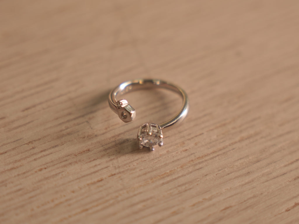 Open sterling silver ring with a round American Diamond in a six prong crown facing a small bezel accent.