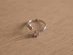 Open sterling silver ring with a round American Diamond in a six prong crown facing a small bezel accent.