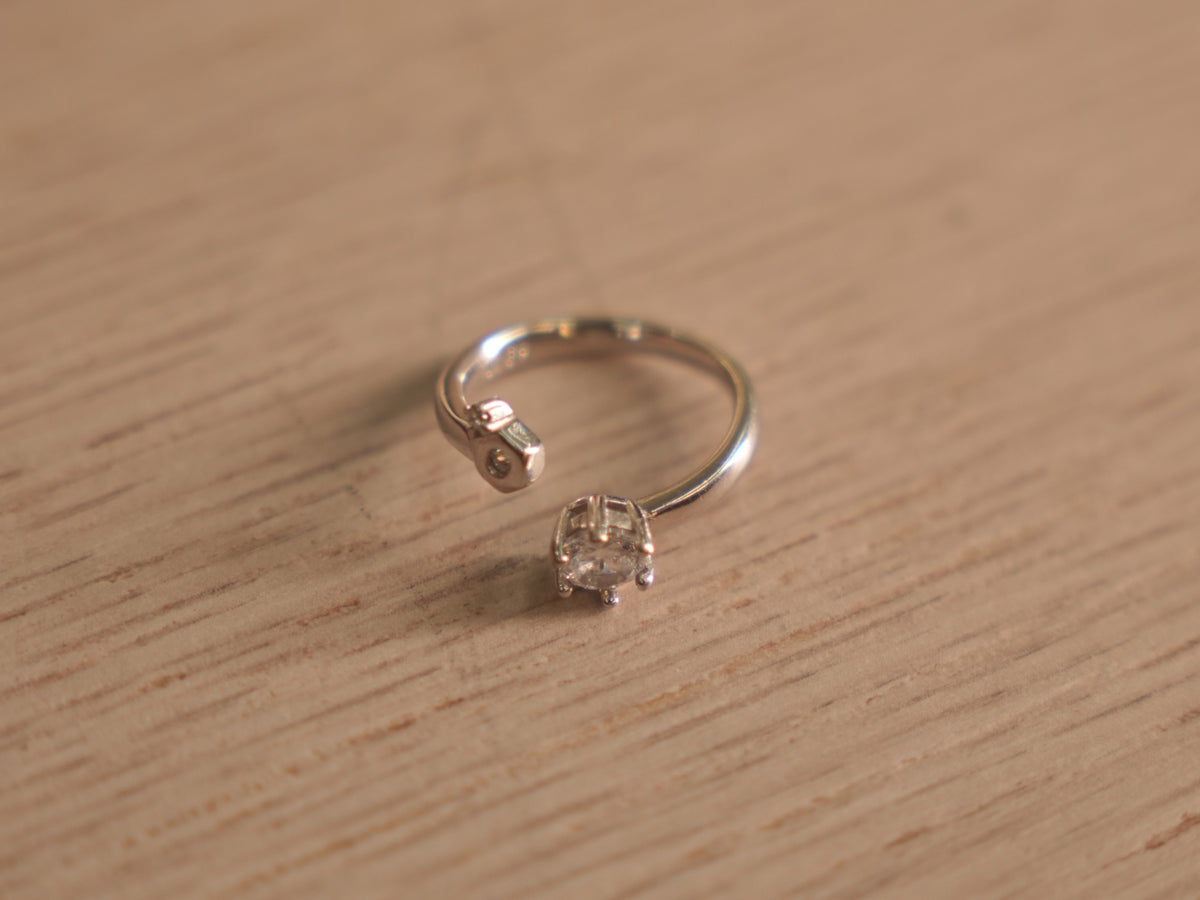 Open sterling silver ring with a round American Diamond in a six prong crown facing a small bezel accent.