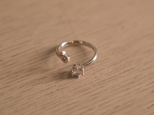 Open sterling silver ring with a round American Diamond in a six prong crown facing a small bezel accent.