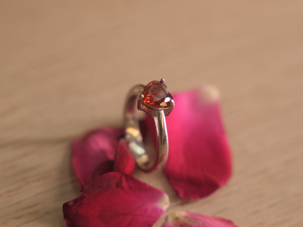 The red heart ring standing upright on a pale wooden surface.