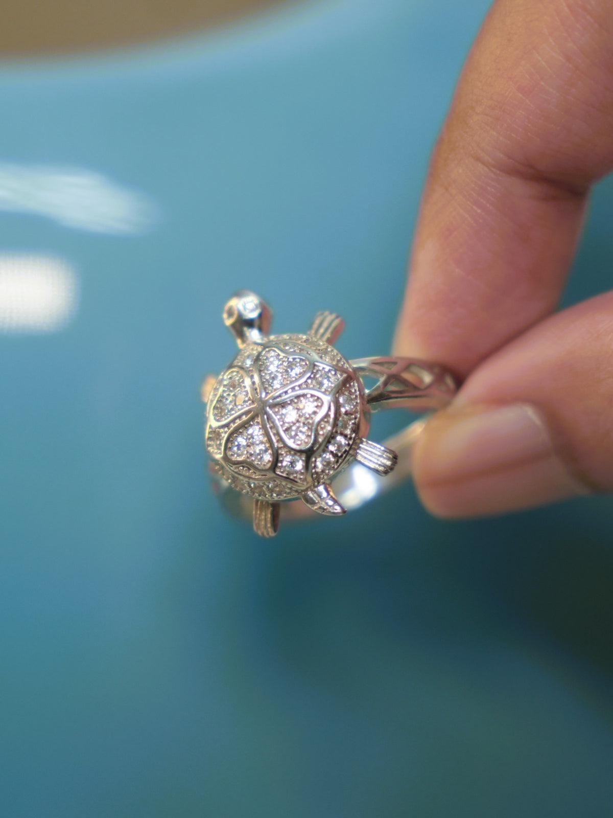 Sterling silver tortoise ring with a four petal American Diamond shell, held against a blue vase.