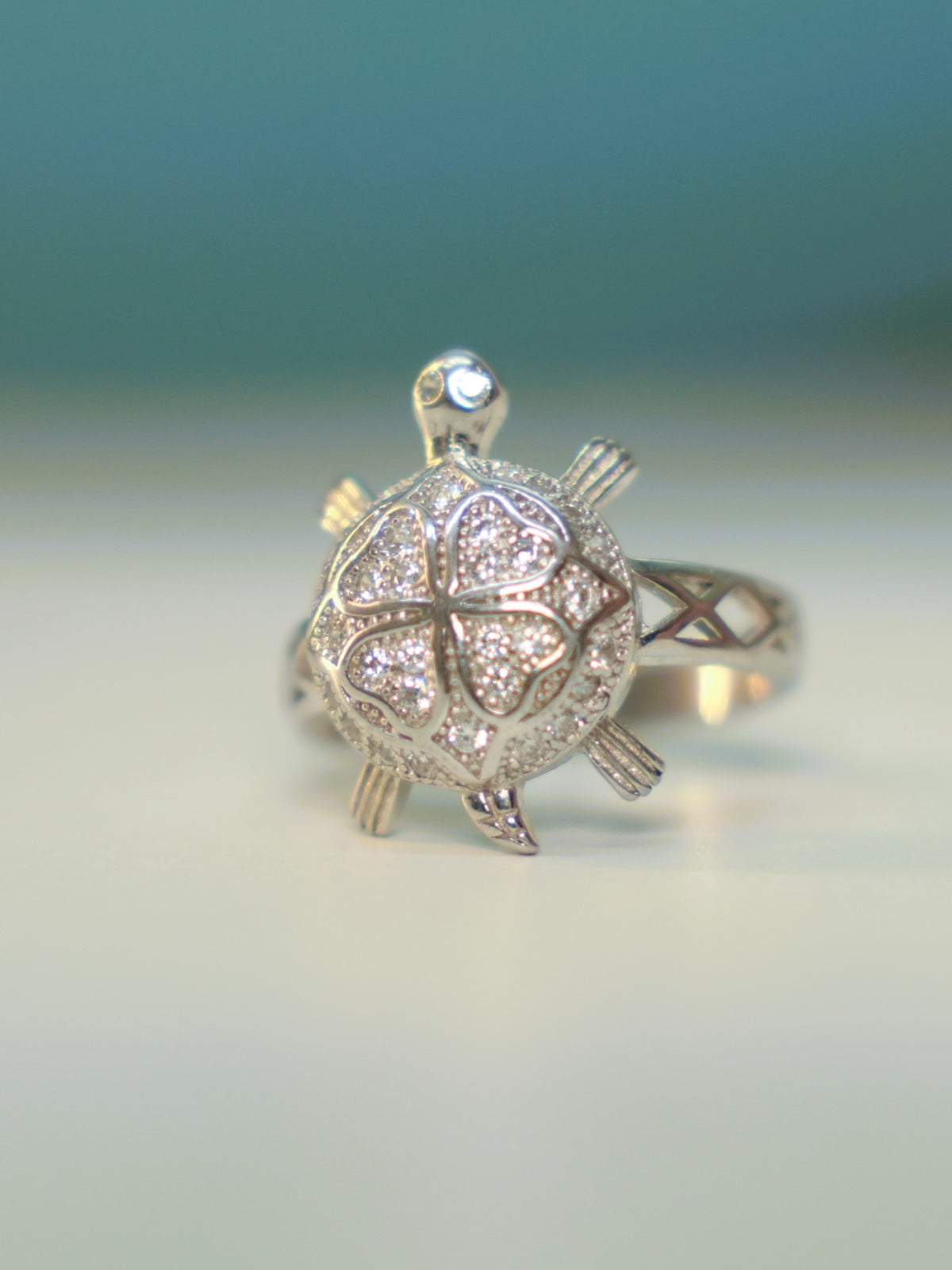 Front view of the four petal tortoise ring standing on a pale surface.
