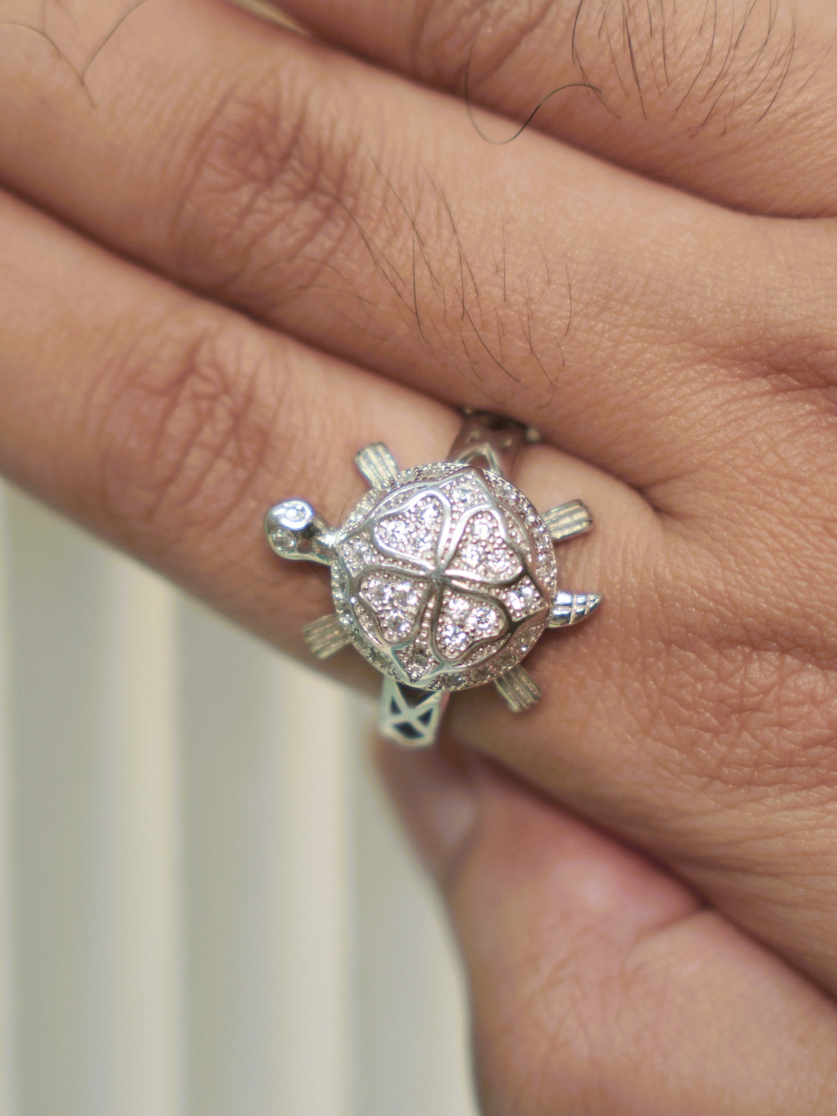 The four petal tortoise ring worn on a hand, showing its scale on the finger.