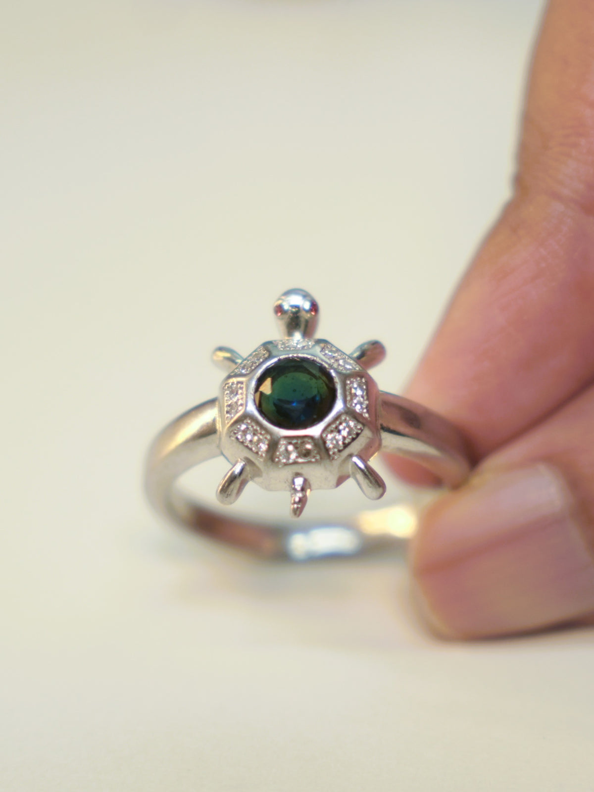Sterling silver tortoise ring with an eight sided shell and a deep blue centre stone, held in the hand.
