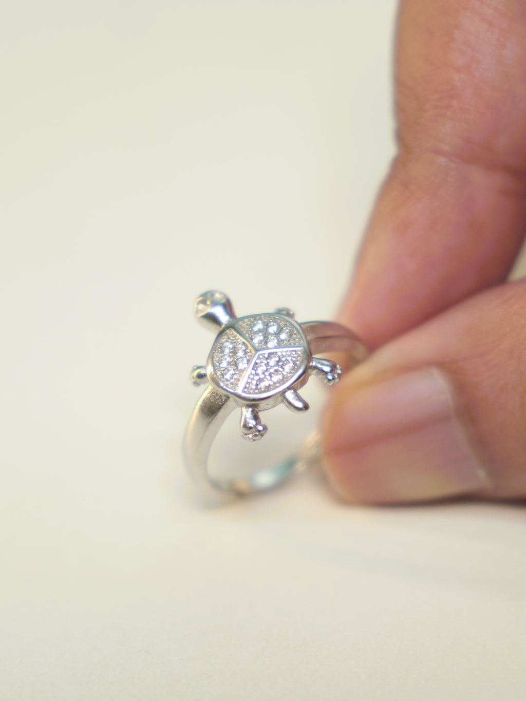 Small sterling silver tortoise ring with an American Diamond pave shell, held between two fingers.
