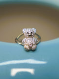 Sterling silver teddy bear ring pave set with American Diamond, with a pink heart at its chest, on the rim of a blue vase.