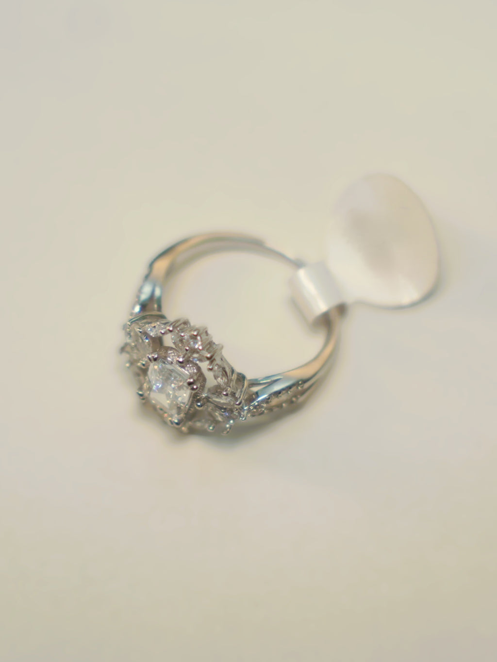 The emerald cut halo ring lying on its side with its size tag attached.