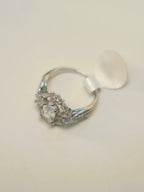 The emerald cut halo ring lying on its side with its size tag attached.