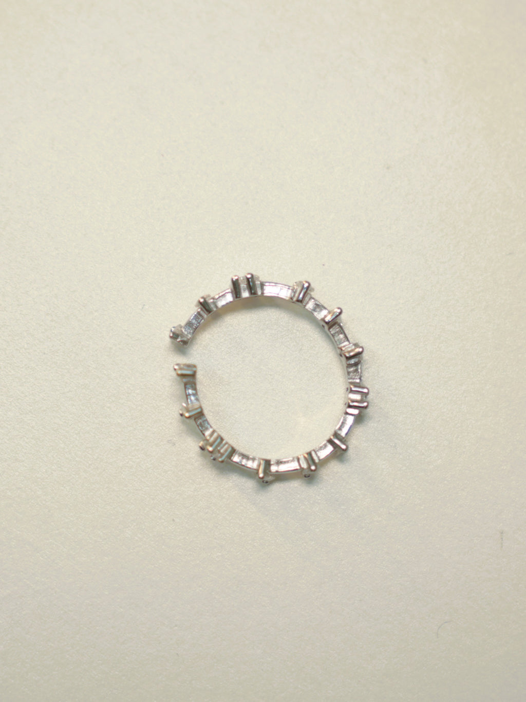 Slim open sterling silver band set with baguette American Diamonds, lying on a pale surface.