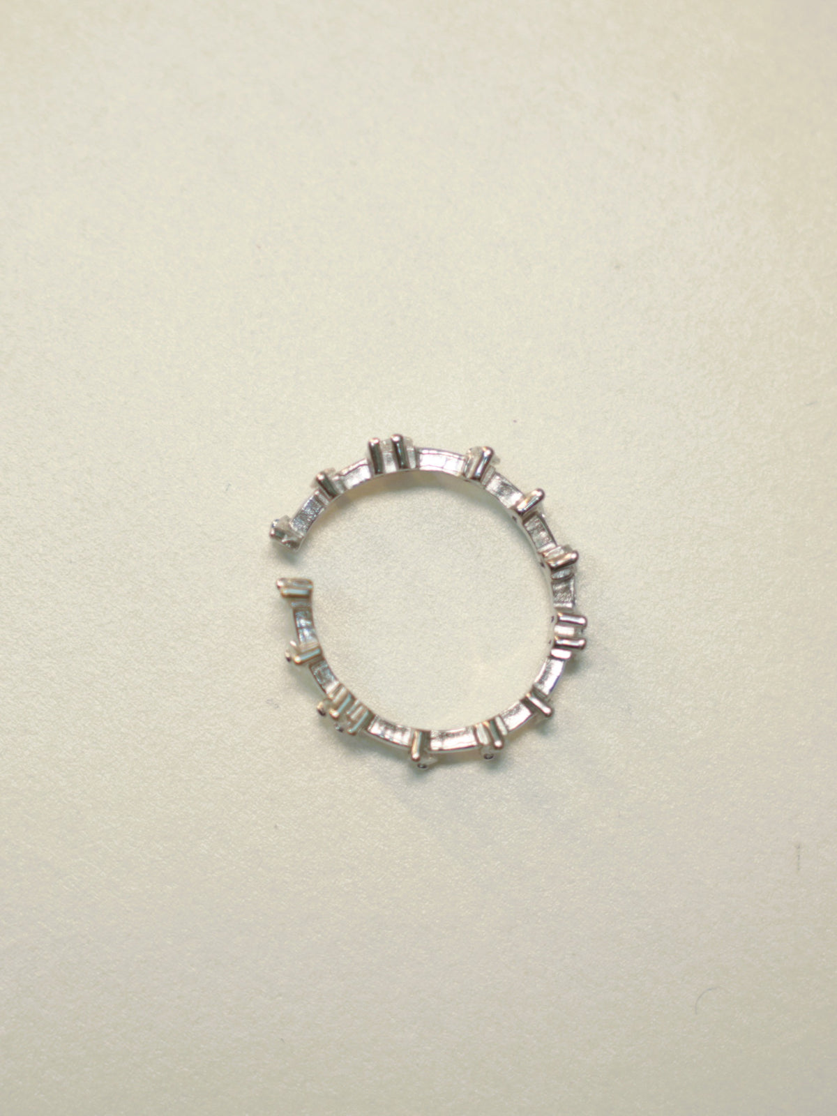 Slim open sterling silver band set with baguette American Diamonds, lying on a pale surface.