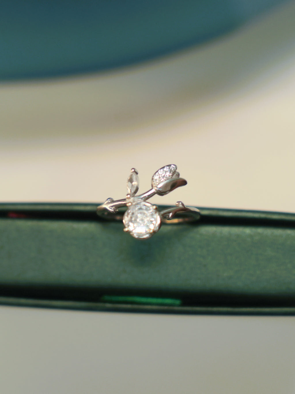 Sterling silver bypass ring with a round American Diamond and a pave set tulip bud, standing on the edge of a green box.