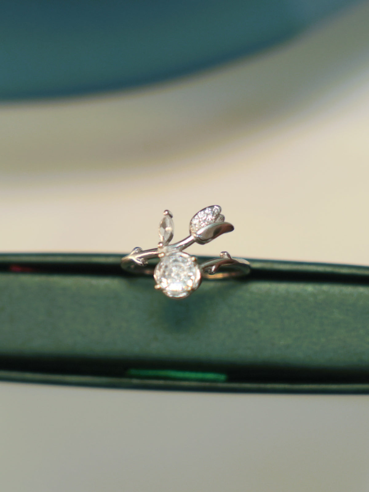 Sterling silver bypass ring with a round American Diamond and a pave set tulip bud, standing on the edge of a green box.