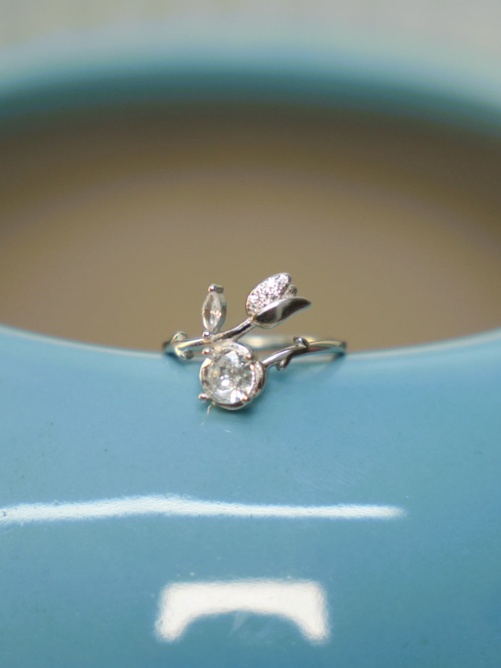 The tulip bud bypass ring resting on the rim of a blue vase.