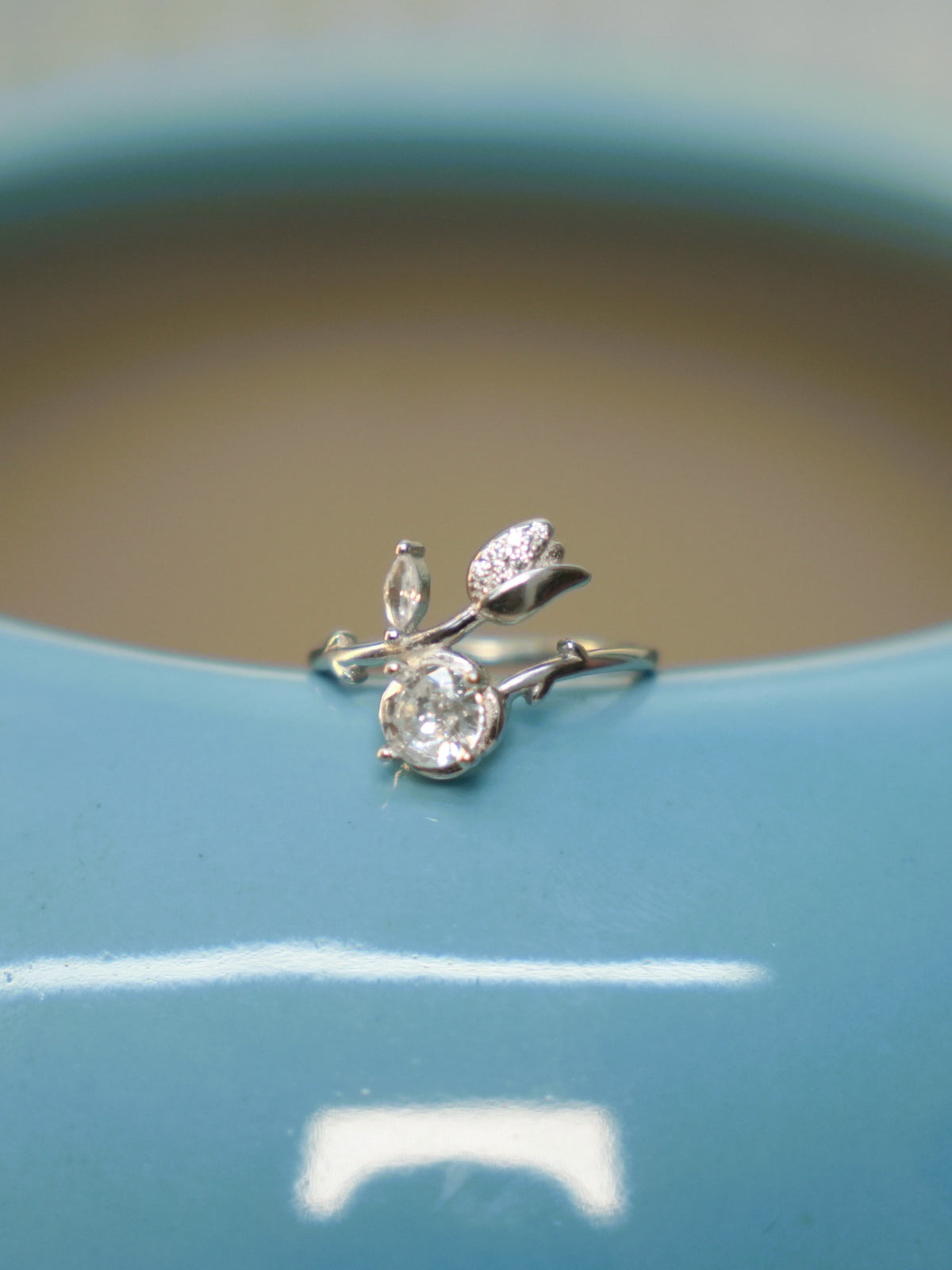 The tulip bud bypass ring resting on the rim of a blue vase.