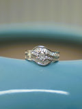 Sterling silver wave ring with a round American Diamond between curved rows of baguette stones, on the rim of a blue vase.