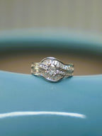 Sterling silver wave ring with a round American Diamond between curved rows of baguette stones, on the rim of a blue vase.