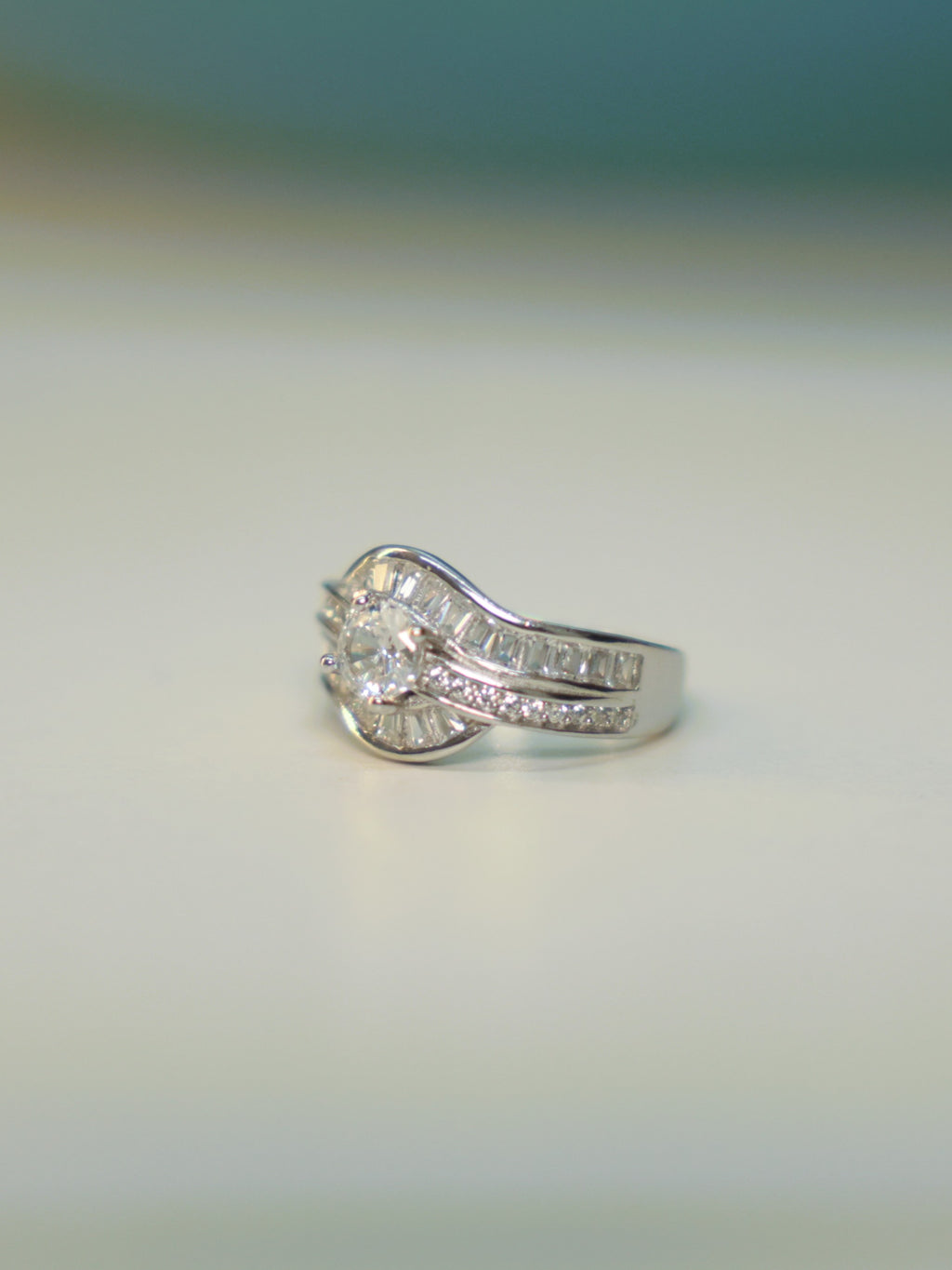 Side view of the wave ring standing on a pale surface, showing the channel set baguettes.