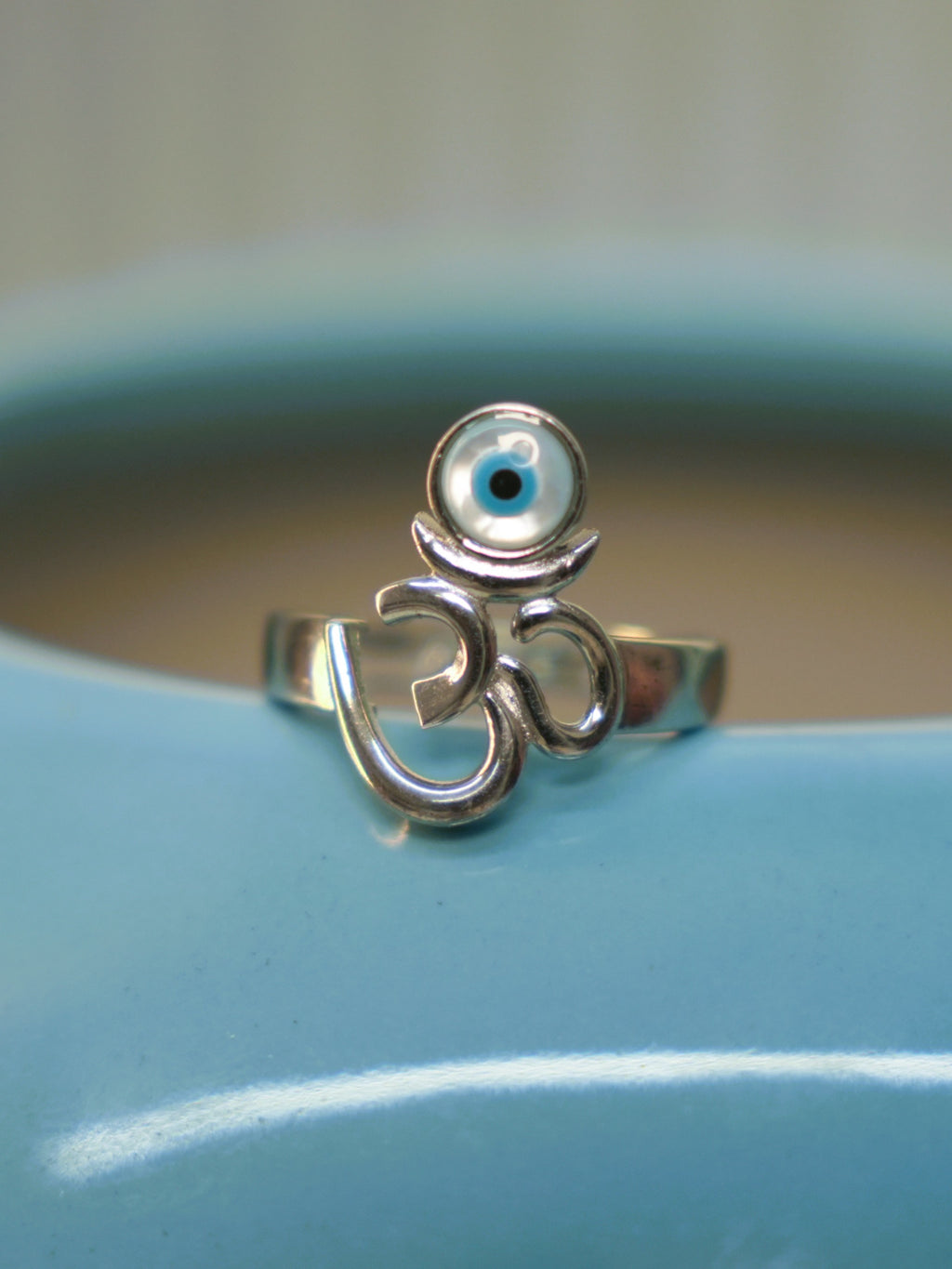 The Om and evil eye ring resting on the rim of a blue vase, seen from the front.