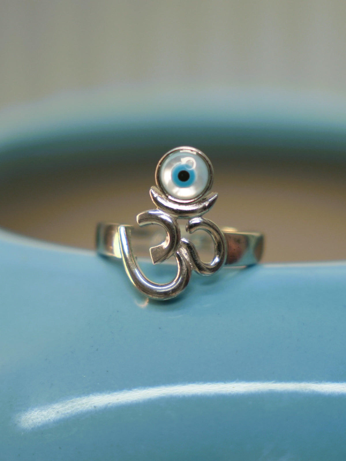 The Om and evil eye ring resting on the rim of a blue vase, seen from the front.
