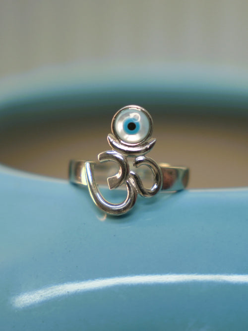 The Om and evil eye ring resting on the rim of a blue vase, seen from the front.