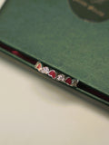 Sterling silver band ring of alternating red enamel hearts and pave set hearts, on the edge of a green box.