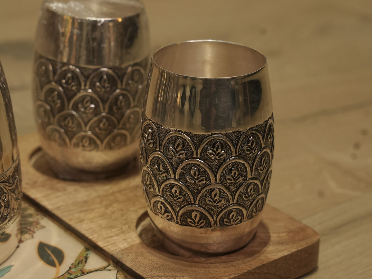 Pair of barrel shaped sterling silver drinking glasses engraved with scallop arches, on wooden coasters.