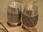 Close view of the engraved band on a silver drinking glass, showing leaf sprays inside darkened arches.