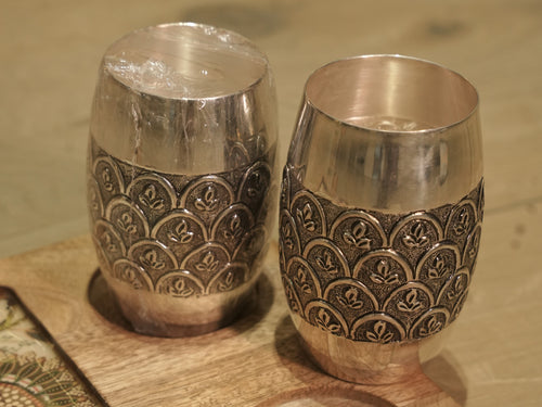 Close view of the engraved band on a silver drinking glass, showing leaf sprays inside darkened arches.