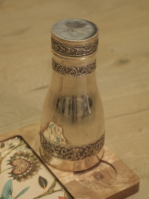 Sterling silver bedside carafe with chased vine bands and a fitted lid, standing on a wooden coaster.