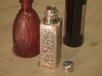 Close view of a flowering vine panel on the square silver bottle.