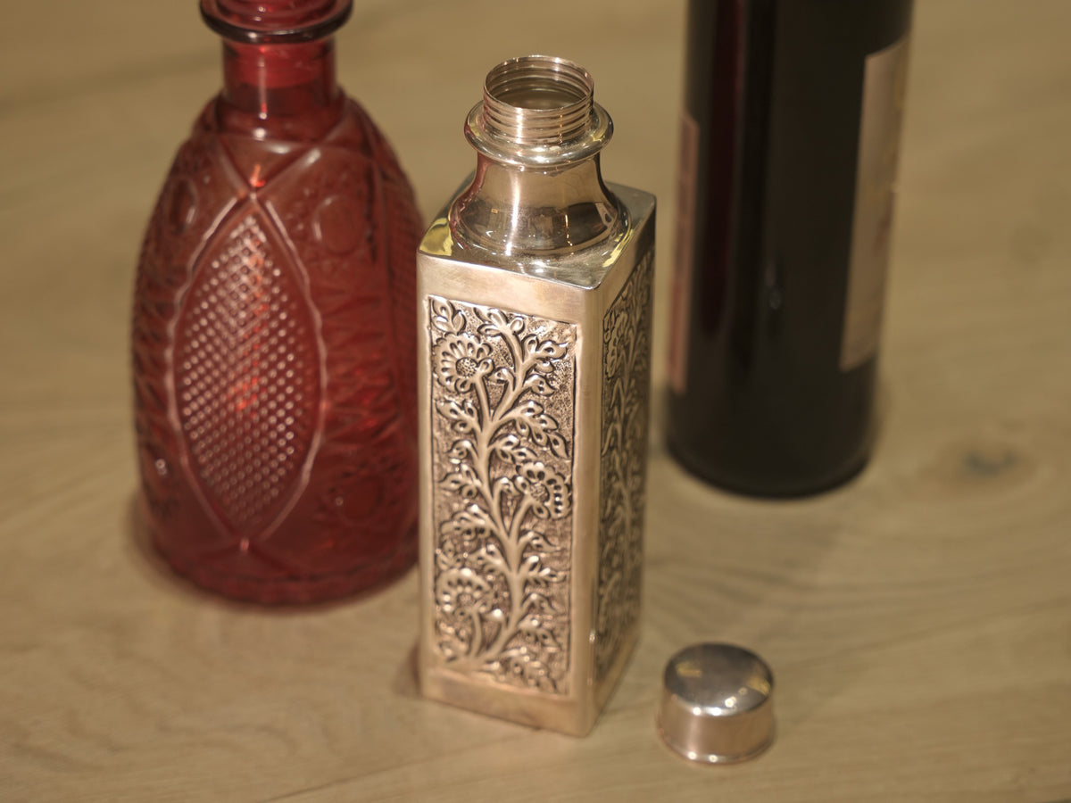 Close view of a flowering vine panel on the square silver bottle.