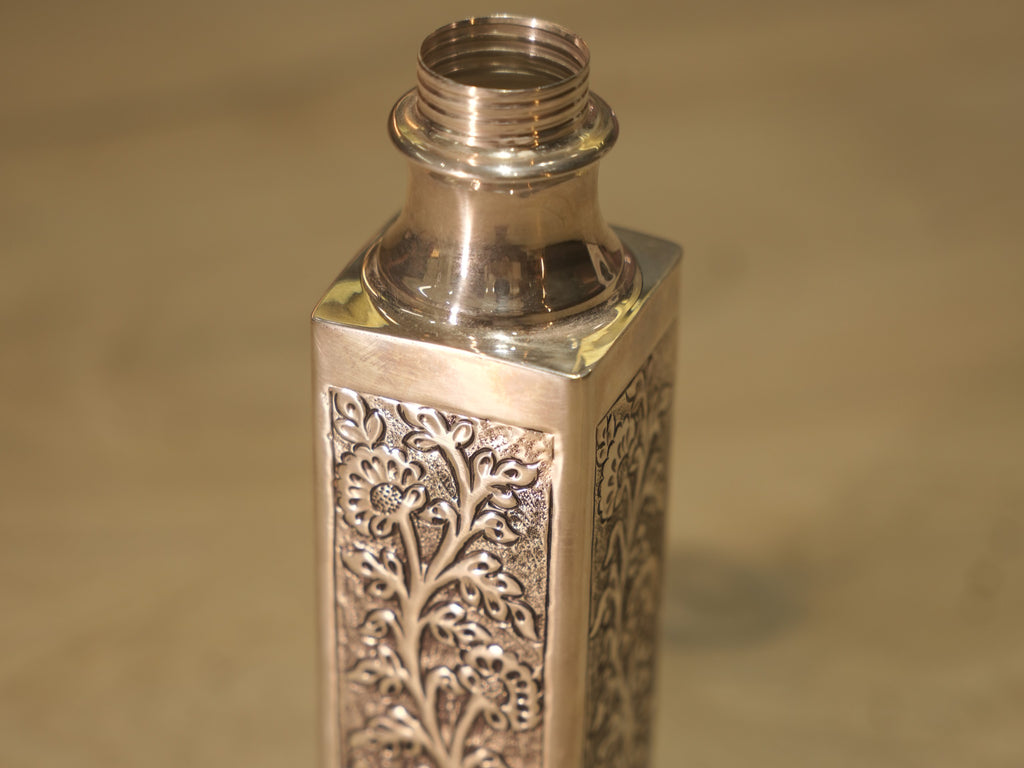The square silver bottle showing two panelled faces and the round threaded neck.
