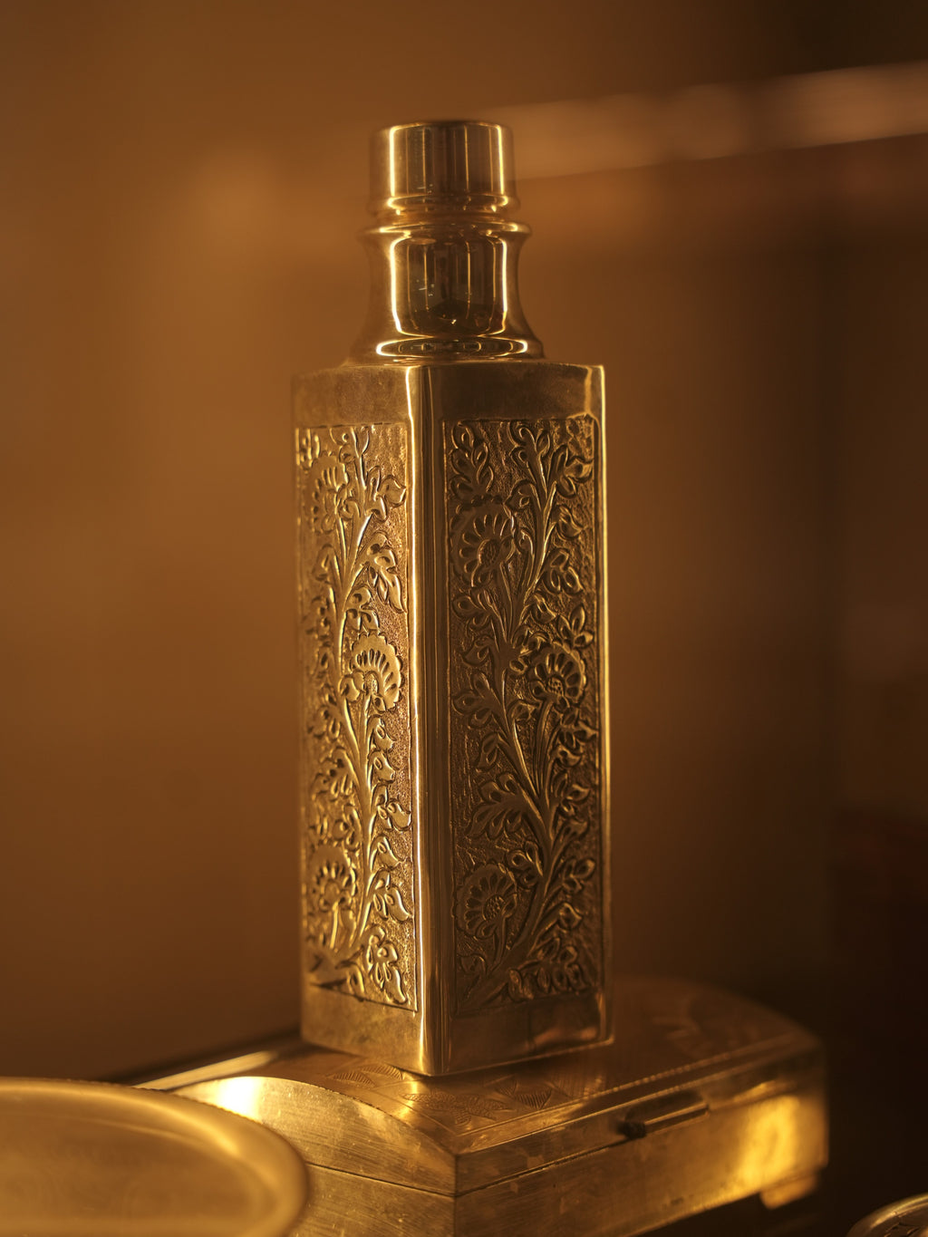 The square silver bottle in warm light, showing the repousse panels on adjoining faces.
