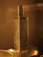 The square silver bottle in warm light, showing the repousse panels on adjoining faces.
